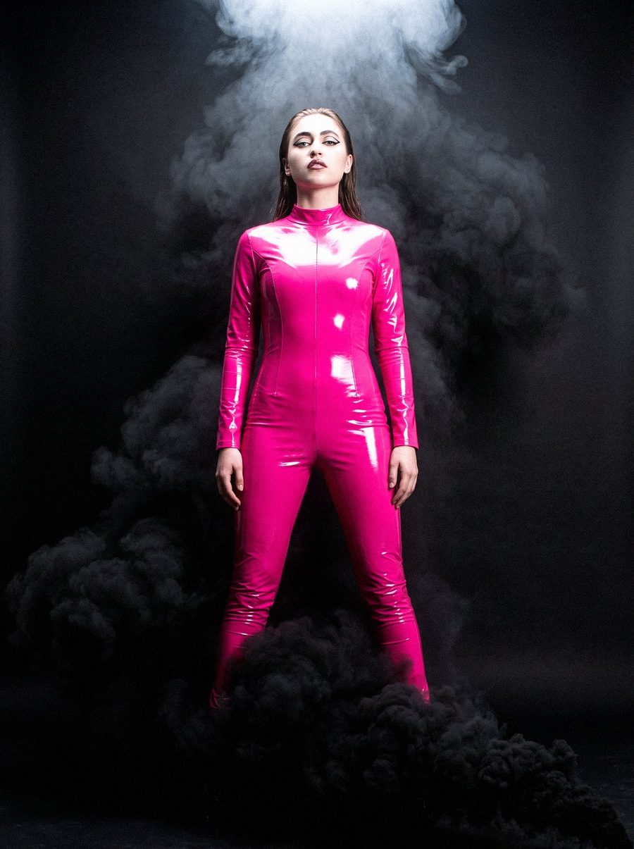 Victoria Grace standing in a pink latex catsuit in black smoke