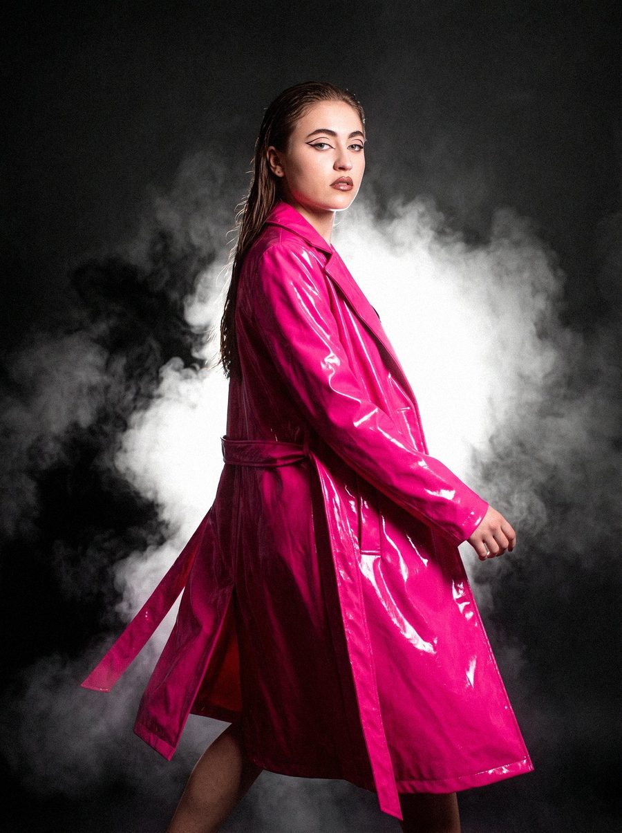 Victoria Grace in a pink patent trench coat against black smoke
