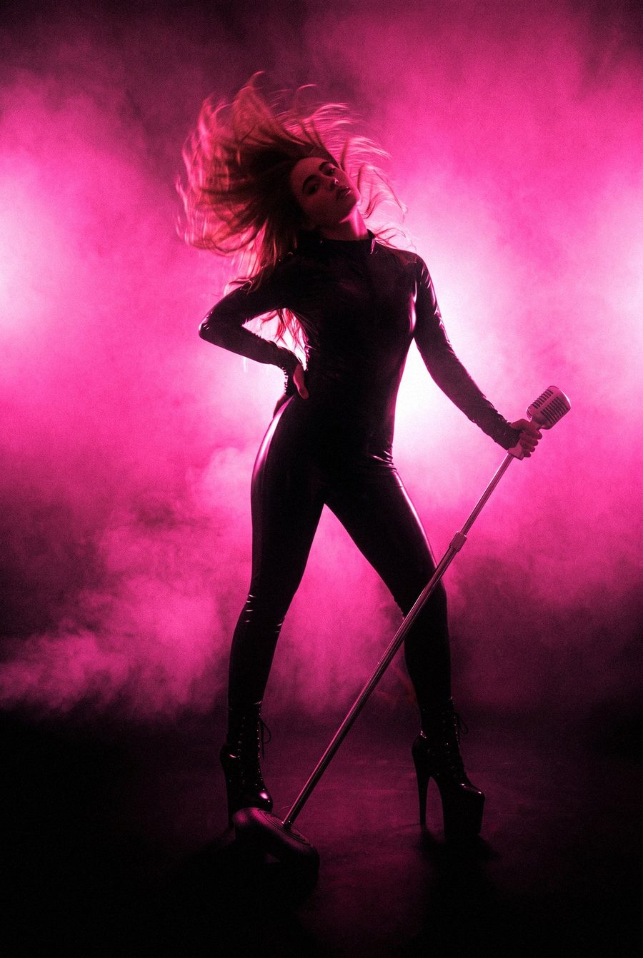 Victoria Grace in silhouette with a microphone stand against a wall of pink light