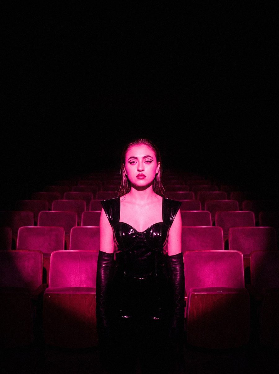 Victoria Grace alone on stage in an empty theatre under a pink spot